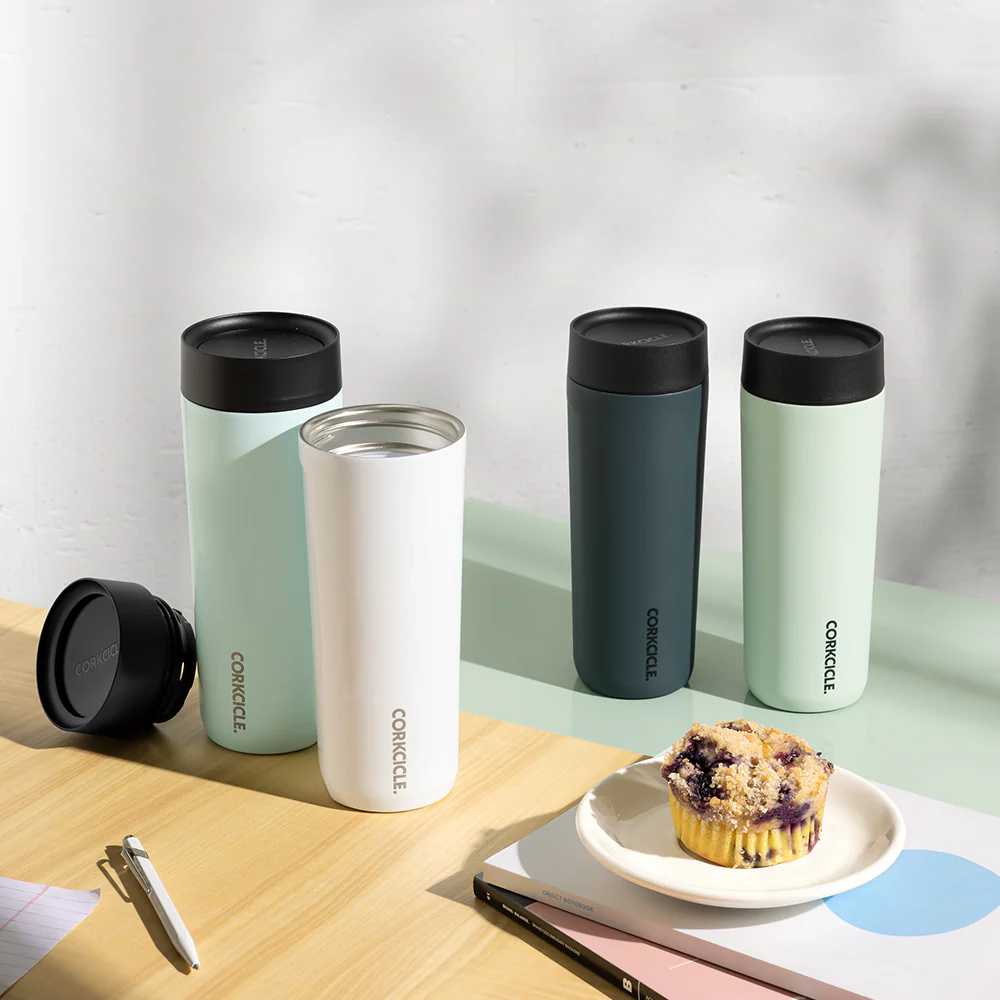 4 corkcicle commuter cups on a table with a muffin and some books