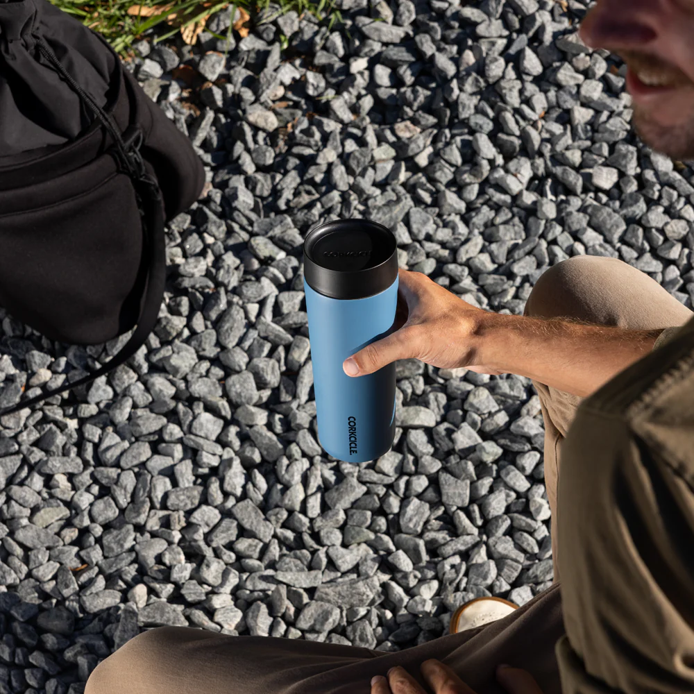man holding corkcicle commuter cup with gravel and a backpack in background